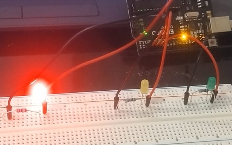 Arduino breadboard project with red, yellow, and green LEDs; red LED is glowing, connected to resistors and an Arduino board via jumper wires.