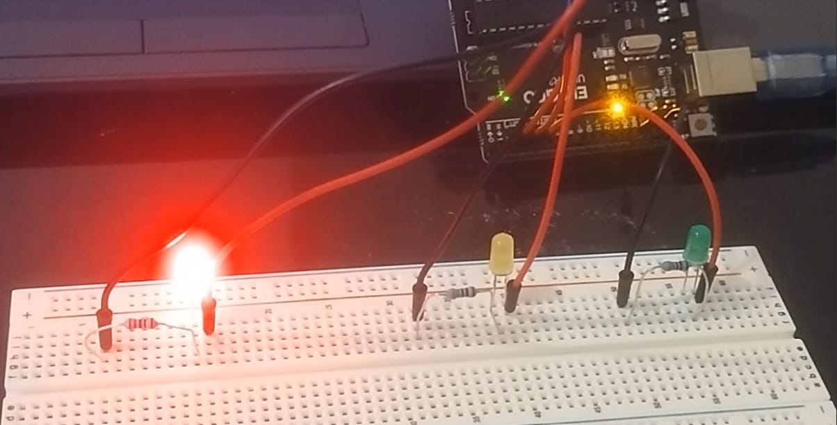 Arduino breadboard project with red, yellow, and green LEDs; red LED is glowing, connected to resistors and an Arduino board via jumper wires.